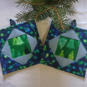 May include: Two blue and green quilted pot holders with a green and white tree design in the center. The pot holders have a loop for hanging.