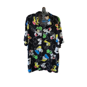 May include: Black button-down shirt featuring a colorful pattern of cartoon characters, including Mickey Mouse, Goofy, and Donald Duck. The short-sleeved shirt has a classic collar and is hanging on a black hanger.