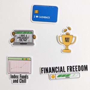 May include: Four colorful stickers with financial themes. The first sticker is blue and says "I ♥ CASHBACK". The second sticker shows a laptop with a spreadsheet and says "I HAVE A SPREADSHEET FOR THAT". The third sticker shows a gold trophy with coins falling into it and says "DEBT FREE". The fourth sticker is black and says "FINANCIAL FREEDOM" with a green progress bar that says "LOADING".