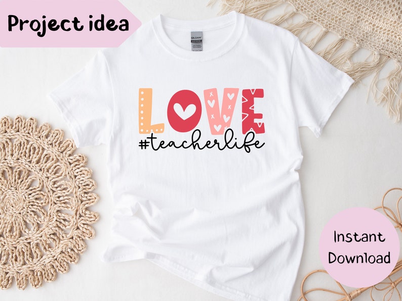 Pu&ograve; includere: Maglietta bianca con la parola "LOVE" in lettere rosse, rosa e arancioni con cuori e altri motivi. Il testo "#teacherlife" &egrave; sotto la parola "LOVE".