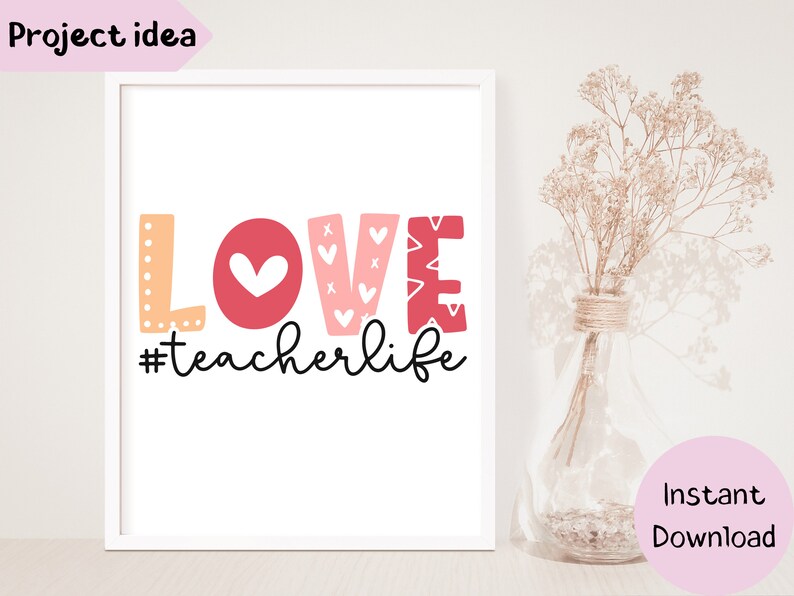 Pu&ograve; includere: Una stampa incorniciata bianca con la parola "LOVE" in lettere rosa e arancioni con cuori e il testo "#teacherlife" in scrittura corsiva nera.