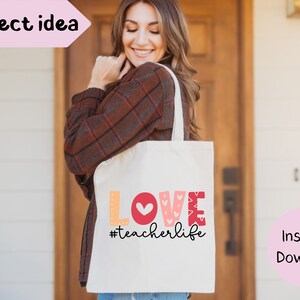 Pu&ograve; includere: Una borsa tote bianca con le parole "LOVE #teacherlife" in lettere colorate e un cuore rosso. La borsa &egrave; tenuta da una persona che indossa una camicia a quadri marroni.