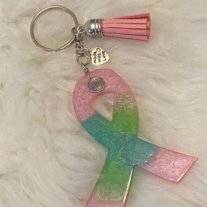 Pu&ograve; includere: Un portachiavi a forma di nastro rosa e verde glitterato con un ciondolo argentato che dice "made with love". Il portachiavi ha anche un pon pon rosa.