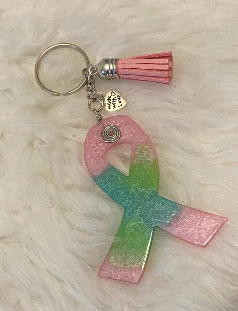 Pu&ograve; includere: Un portachiavi a forma di nastro rosa e verde glitterato con un ciondolo argentato che dice "made with love". Il portachiavi ha anche un pon pon rosa.