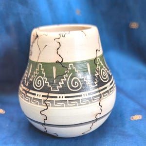 May include: A small, rounded ceramic vase with a cream-coloured base featuring black horsehair-style crackle patterns. The midsection displays a horizontal band of green and dark grey with etched geometric spiral and Greek key motifs.