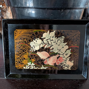 May include: A black lacquer tray with a gold and red floral design and two birds. The tray has a raised rim and a smooth surface.