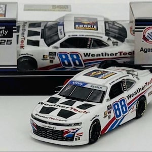 May include: A white and blue WeatherTech NASCAR Xfinity Series race car model with the number 88. The model is in front of its box, which also features the car. The box reads "Ages 6+".