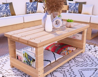 Puede incluir: Una mesa de centro de madera clara con un estante inferior que contiene cojines y revistas. La mesa está rodeada de muebles de exterior blancos y una alfombra estampada. Jarrones decorativos y plantas se encuentran sobre la mesa.
