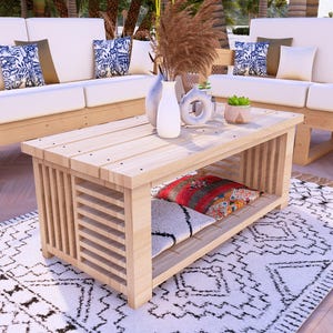 May include: A light-coloured wooden coffee table with a slatted side design and a lower shelf. The table is surrounded by white sofas with patterned cushions, a patterned rug, and decorative vases. The table measures approximately 122 cm long, 61 cm wide, and 46 cm high.