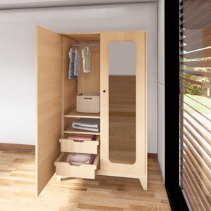 May include: A light wood wardrobe with two doors, one with a mirror. The wardrobe has two drawers and a shelf with a wicker basket and folded clothes. There are clothes hanging on a rod inside the wardrobe.