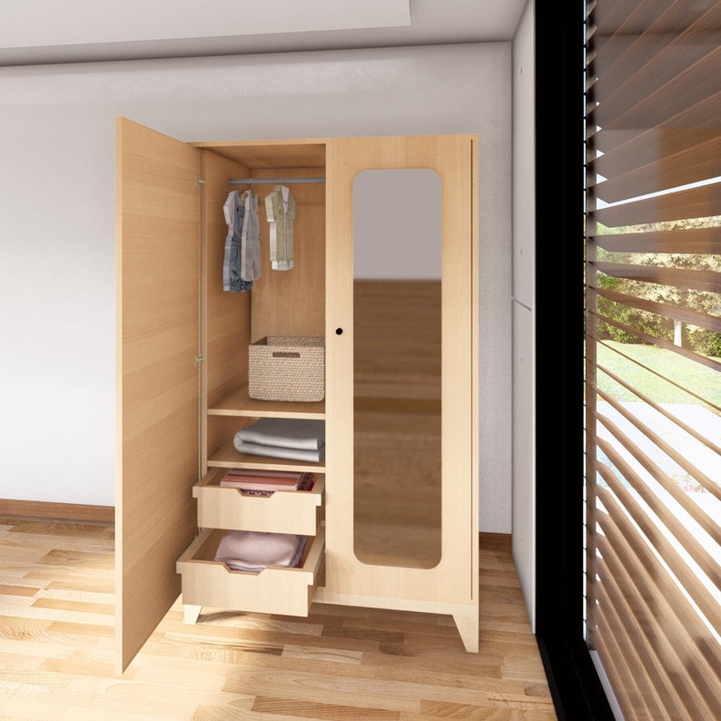 May include: A light wood wardrobe with two doors, one with a mirror. The wardrobe has two drawers and a shelf with a wicker basket and folded clothes. There are clothes hanging on a rod inside the wardrobe.