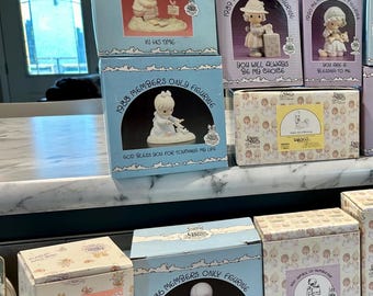 May include: A collection of blue and white boxes with Precious Moments figurines. The boxes are stacked on a shelf and each box features a different figurine and inscription. The inscriptions include "In His Time", "You Will Always Be My Choice", "You Are A Blessing To Me", "God Bless You For Touching My Life", and "Grandma's Prayer".