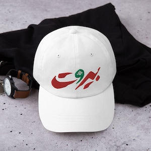 May include: White baseball cap with embroidered Arabic text in red and green. The cap features a curved brim and a classic six-panel design. The text appears to be a city name.