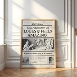 May include: A framed vintage-style advertisement for a spray tan service. The black and white print features the headline "Local girl gets spray tan LOOKS & FEELS AMAZING." The image includes a woman receiving a spray tan and additional text.