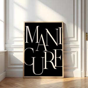 Può includere: Una stampa artistica incorniciata con la parola "MANICURE" in un grande carattere serif bianco su sfondo nero. L'opera d'arte è esposta in una stanza con pareti bianche, una finestra e un pavimento in legno. La cornice è di colore marrone chiaro.