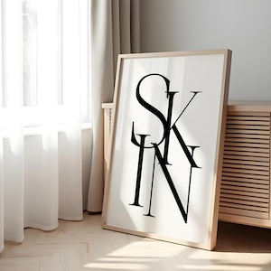Può includere: Una stampa artistica incorniciata con la parola "SKIN" in lettere nere e in grassetto su sfondo bianco. L'opera d'arte è in una cornice di legno chiaro ed è appoggiata vicino a una finestra con tende trasparenti.