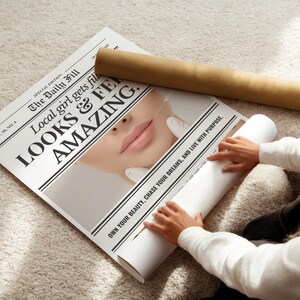Puede incluir: Un p&oacute;ster estilo peri&oacute;dico con el titular "Local girl gets fill LOOKS & FE AMAZING." El p&oacute;ster se est&aacute; enrollando, con un tubo marr&oacute;n y un tubo blanco visibles. Tambi&eacute;n es visible el texto "OWN YOUR BEAUTY, CHASE YOUR DREAMS, AND LIVE WITH PURPOSE".