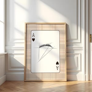 May include: Framed art print of the Ace of Hearts playing card. The card features a minimalist black and white illustration of an eye and geometric lines. The frame has a plaid pattern.