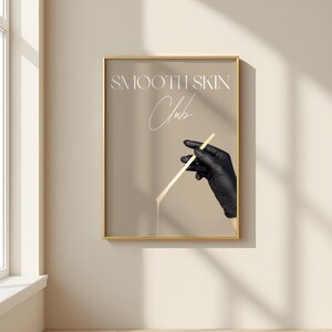 Op de afbeelding: Een poster met een gouden lijst en een beige achtergrond. De poster toont een zwarte, handschoen-geklede hand die een houten stok vasthoudt met een witte substantie die er vanaf druppelt. De tekst "SMOOTH SKIN Club" is in wit op de poster geschreven.