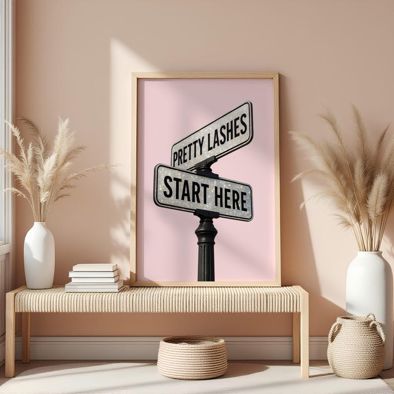 May include: A framed print featuring a pink background with two street signs that read "Pretty Lashes" and "Start Here." The signs are mounted on a black post. The print is displayed above a woven bench with decorative vases.