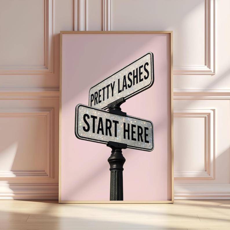 May include: A framed print featuring a street sign design with the words "PRETTY LASHES" and "START HERE" in black text on a silver glitter background. The sign is mounted on a black post against a pink backdrop.