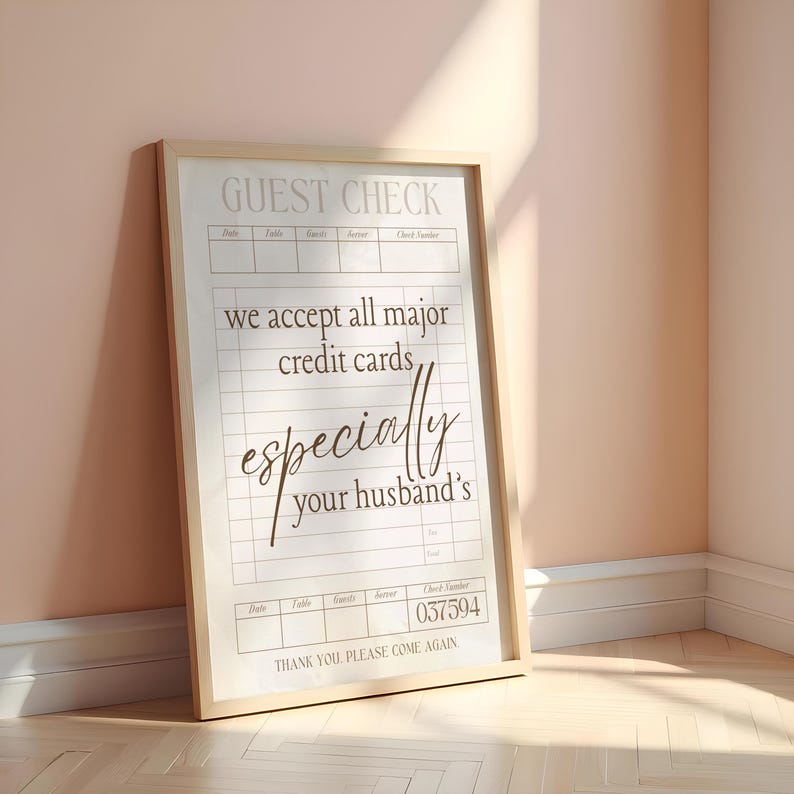 May include: A framed "Guest Check" sign with a light wood frame. The sign has a grid layout with text that reads "we accept all major credit cards, especially your husband's." The check number is 037594.