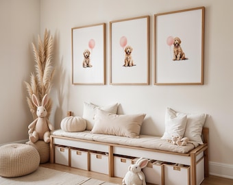 May include: Three framed prints of a golden retriever puppy holding a pink balloon hang above a bench with white storage drawers. The room is decorated with neutral tones, including a beige ottoman, a stuffed bunny, and decorative pampas grass.