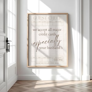 May include: A framed print with a light wood frame. The print is designed to look like a guest check, with the text "GUEST CHECK" at the top. The text reads "we accept all major credit cards, especially your husband's".