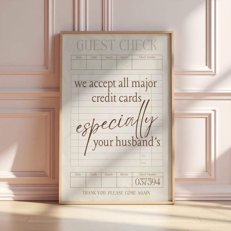 May include: A framed guest check print with a beige background and a gold frame. The text reads "GUEST CHECK" at the top, followed by "we accept all major credit cards, especially your husband's." The check number is 037594.