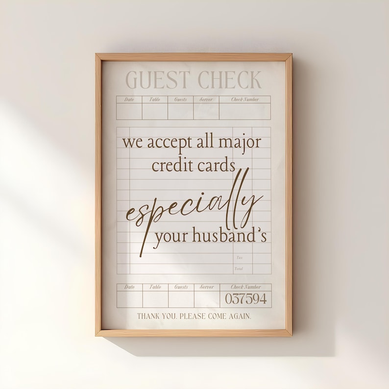 May include: A framed guest check print with a light wood frame. The text reads "GUEST CHECK" at the top, followed by lines for details. The print humorously states "we accept all major credit cards, especially your husband's." The check number is 037594.