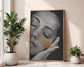 May include: Black and white framed art print featuring a grayscale portrait of a person with closed eyes and gold glitter eye patches. The person's hand gently rests on their cheek. The artwork is displayed in a room with plants.