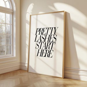 Puede incluir: Una lámina de arte mural rectangular en un marco dorado fino con el texto negro PRETTY LASHES START HERE en una fuente serif negrita sobre un fondo crema. La obra se muestra en orientación vertical con un diseño limpio y sencillo.