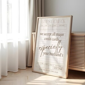 May include: A framed print with a light wood frame. The print is a mock guest check with the text "we accept all major credit cards, especially your husband's." The check number is 037594.