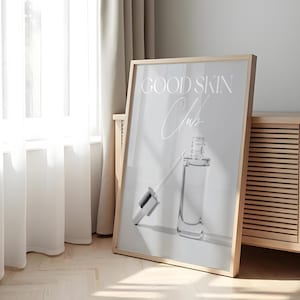 Può includere: Una stampa incorniciata con il testo "GOOD SKIN Club" in lettere bianche su uno sfondo grigio chiaro. Una bottiglia di vetro trasparente con un contagocce si trova nell'angolo in basso a destra della stampa.