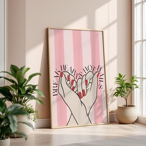 Puede incluir: Un cuadro enmarcado con un fondo a rayas rosas y blancas. La obra de arte representa dos manos formando un corazón, con esmalte de uñas rojo. El texto dice "Break Hearts Not Nails."