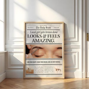 May include: A framed newspaper-style print with the headline "The Daily Brow." The text reads "Local girl gets brows done LOOKS & FEELS AMAZING." The image shows a close-up of an eyebrow being groomed. The bottom text says "OWN YOUR BEAUTY, CHASE YOUR DREAMS, AND LIVE WITH PURPOSE."