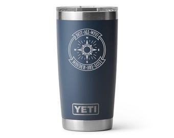 May include: Navy blue insulated tumbler with a silver rim and lid. The tumbler features a white compass design with the text "NOT ALL WHO WANDER ARE LOST." The brand name "YETI" is displayed at the bottom.