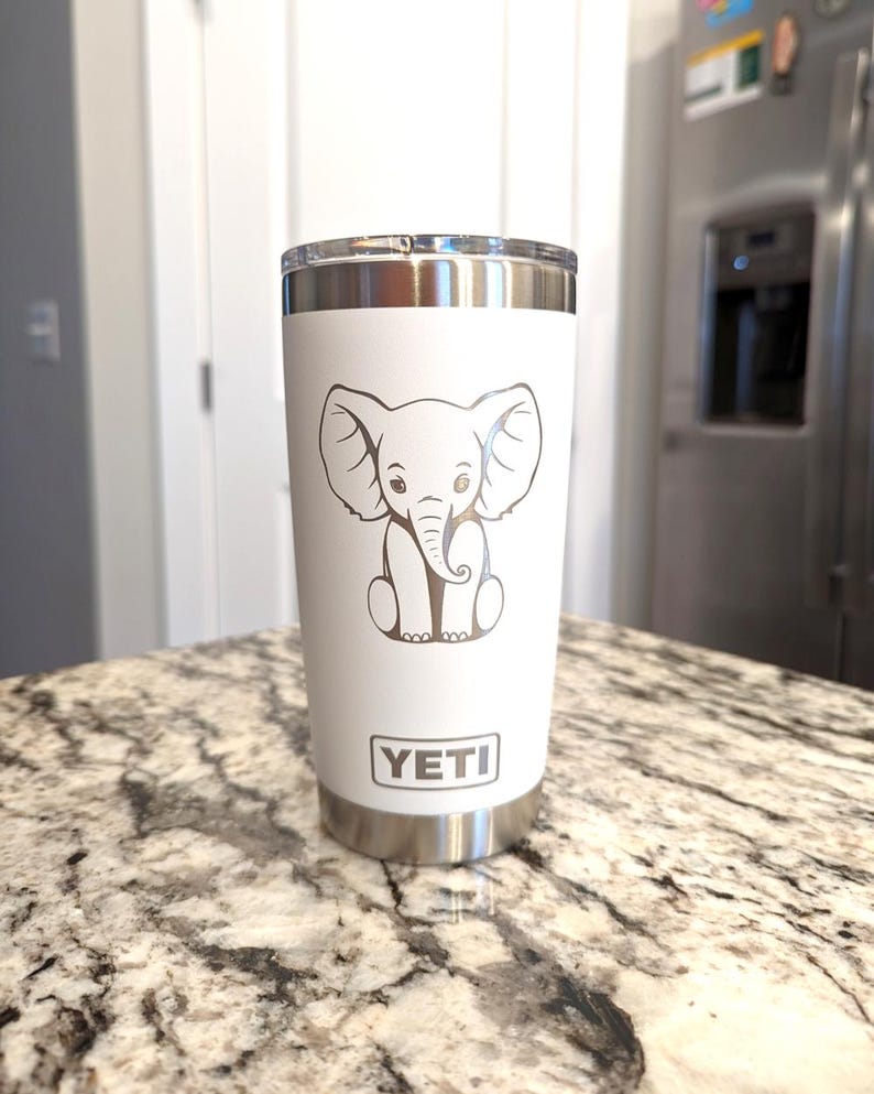 A white 20oz Yeti Rambler Tumbler laser etched with a sitting elephant. The tumbler is a play on a white elephant gift.