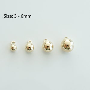 May include: Three gold-coloured metal ball charms of different sizes, measuring 3-6 mm. The charms have a loop at the top for attaching to jewellery or other crafts.