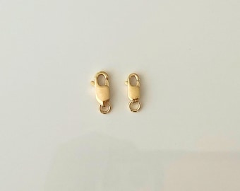 May include: Two gold-toned lobster clasps, one larger than the other, on a white background.