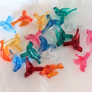 May include: Assortment of colourful plastic bird ornaments for a Christmas tree. The birds are in various colours, including red, blue, green, yellow, and orange.