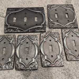 May include: Set of seven decorative light switch covers in a rustic, hammered metal style. The covers feature a raised, ornate design with a silver finish.