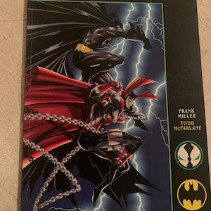 May include: A comic book cover featuring Spawn and Batman fighting. The cover is black with the title "Spawn Batman" in white text. The image shows Spawn in red and black, with chains, and Batman in black and yellow. The cover also includes the names of the creators: Frank Miller, Todd McFarlane, and Image Comics.