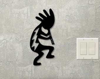 May include: Black metal wall art depicting a Native American Kokopelli figure playing a flute. The figure is stylized and has a distinctive headdress.