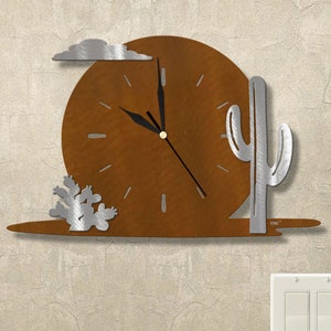 May include: A brown metal wall clock with a cactus and cloud design. The clock face is surrounded by a metal frame with a cactus and cloud design. The clock hands are black.