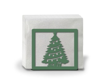 May include: A stack of white paper napkins held by a green metal napkin holder. The holder features a cut-out design of a Christmas tree with ornaments and presents at the base. The design is set within a rectangular frame.