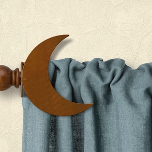 May include: A decorative curtain rod with a crescent moon accent. The rod is made of wood and metal, with a dark brown finish. The curtain is a light blue fabric with vertical stripes.