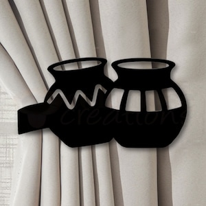 May include: Black metal curtain tiebacks shaped like two stylized pots. The tiebacks are attached to a curtain with a fabric loop.