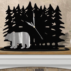 May include: Black metal clock with a silhouette of a bear and pine trees. The clock has a silver-colored bear and black hands.