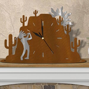 May include: A rustic metal clock with a desert scene featuring a cactus, a mountain, and a sun. The clock face is surrounded by a silhouette of a person playing golf. The clock is on a wooden shelf.